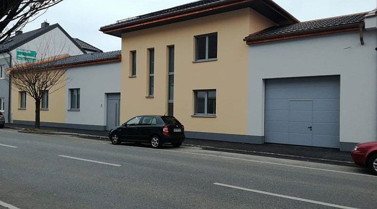 Straßenansicht mit Garageneinfahrt und Hauseingang mit schöner Farbarchitektur in Apricot und Hellgrau.
