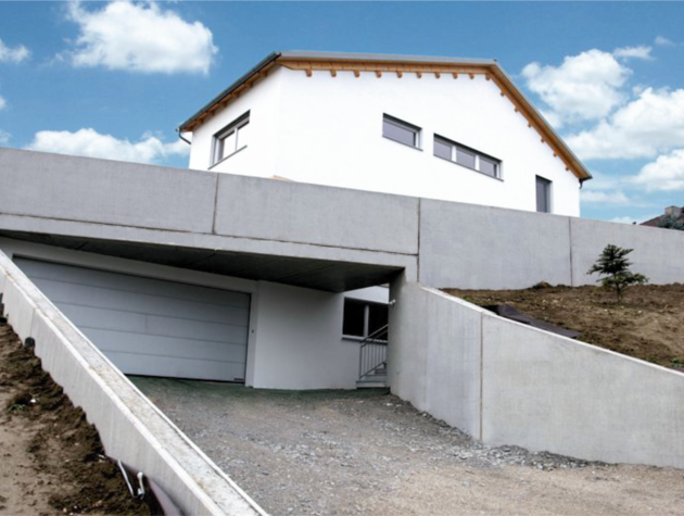 Haus mit Satteldach am Hang mit Garageneinfahrt und Zugang über Keller.